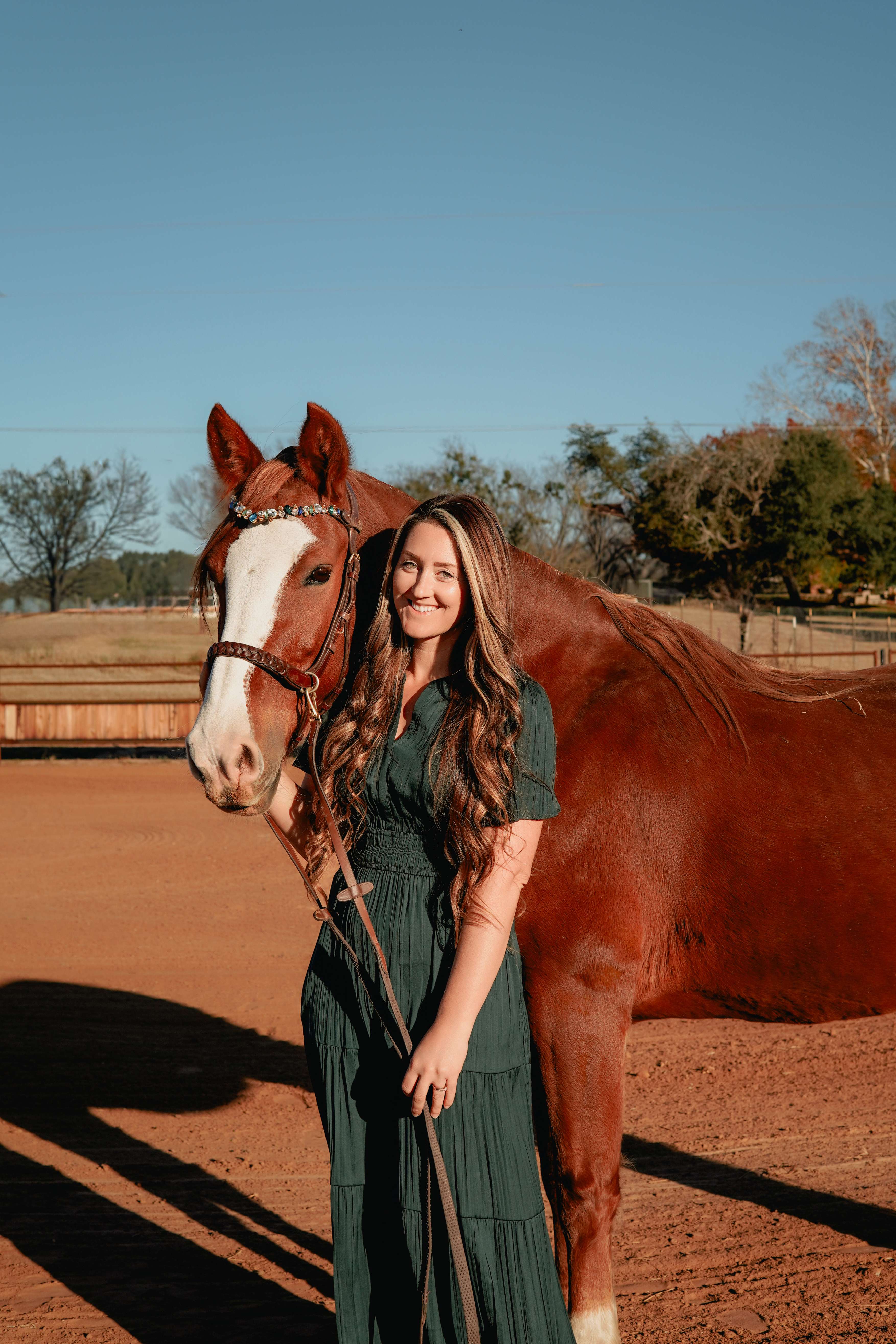 Marina in a green dress smiling beside her chestnut horse in an arena